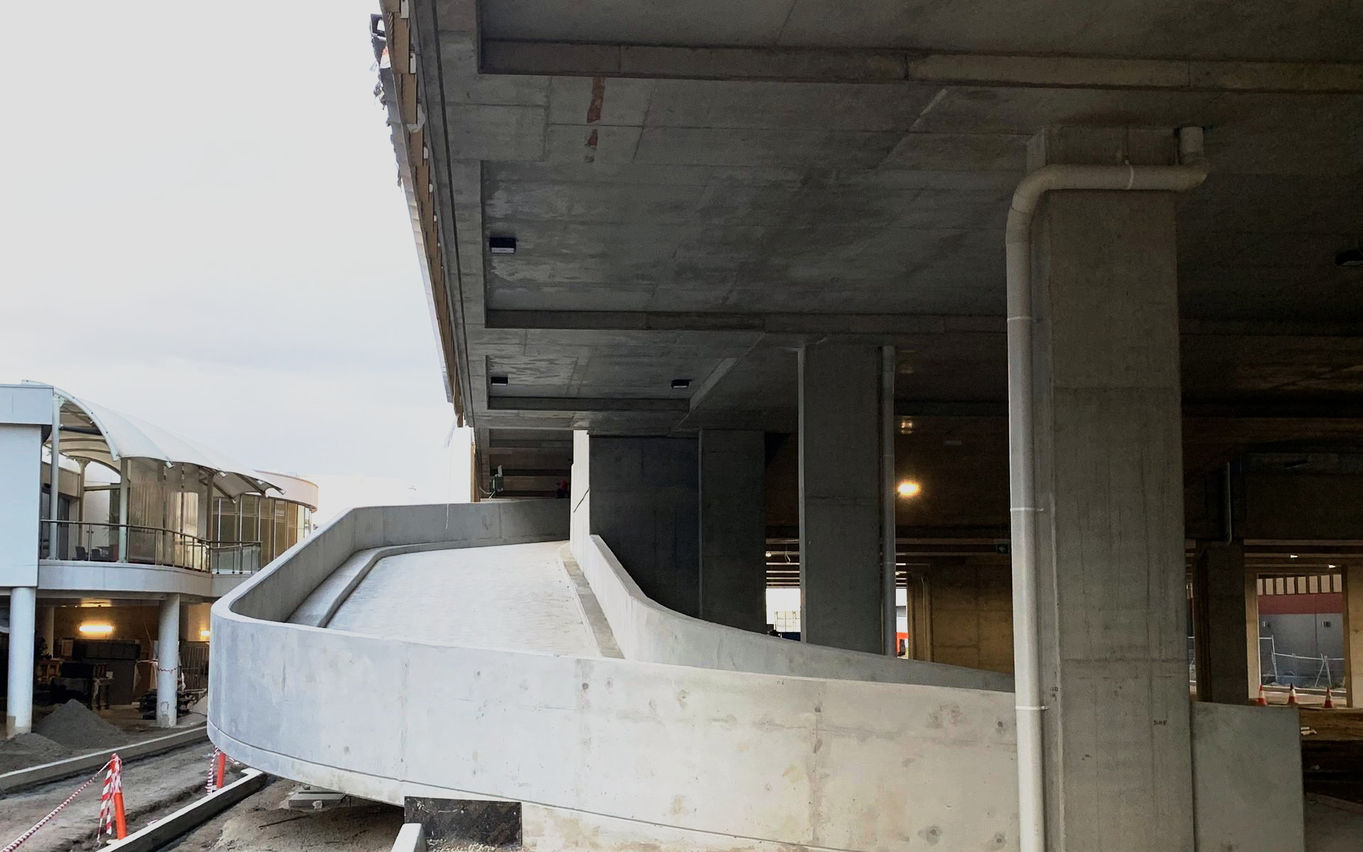 Curved off-form ramp wall sweeping beneath the suspended deck of a multi-level carpark under construction